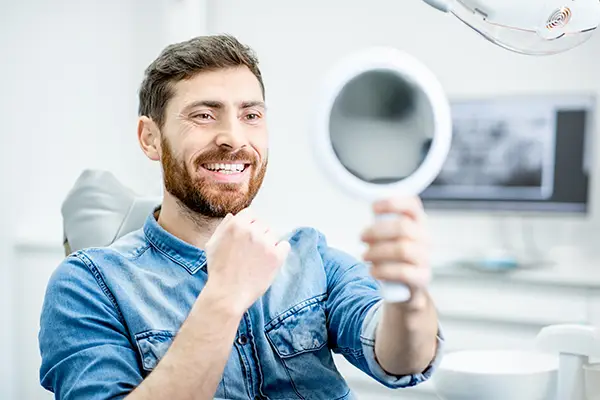 Bearded patient checking out his handsome smile in a mirror, while sitting in a dental chair, at McHenry Smile Center.