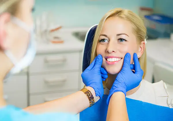 A dentist wearing blue gloves checking a female patient's smile in a dental clinic, showcasing professional dental care.